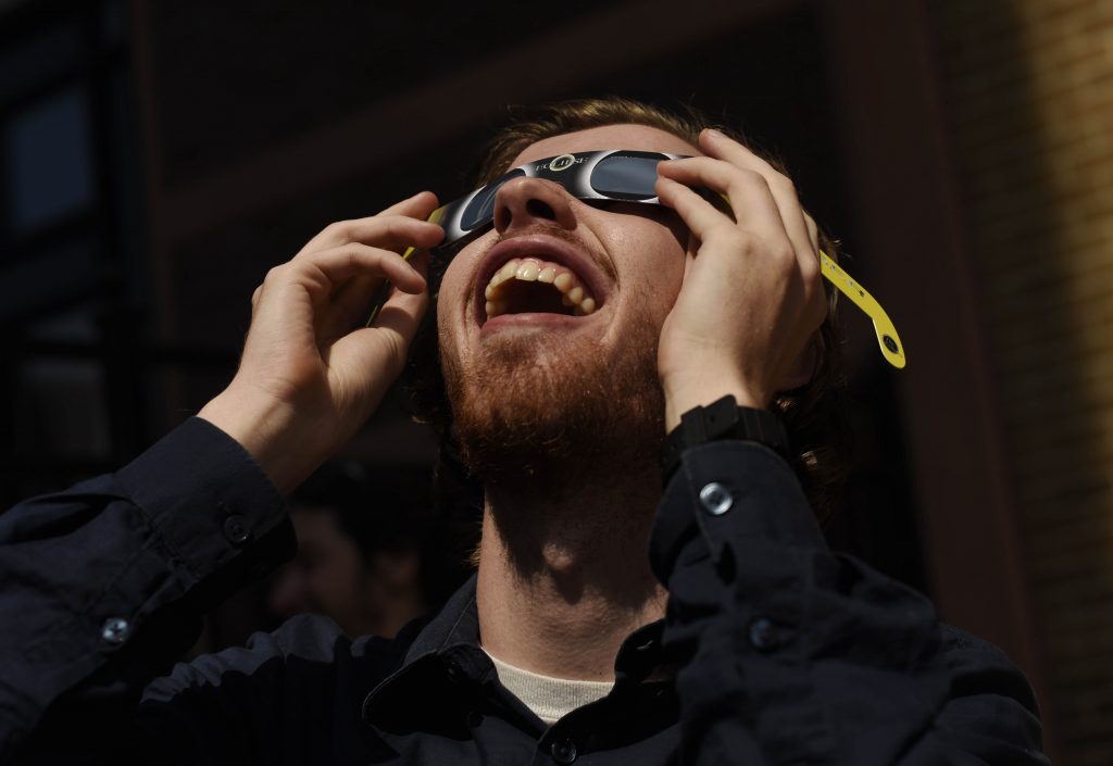 Proctors staff members share Moon Pies and specialty glasses while watching the peak of the eclipse behind the theatre in Schenectady Friday, August 21, 2017.