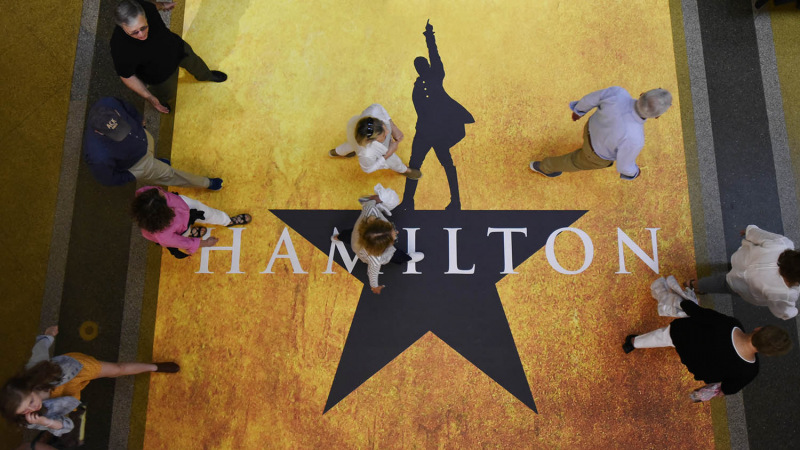 Patrons walk across a special Hamilton floor decal in the arcade in front of the MainStage entrance before the show Thursday, August 15, 2019.